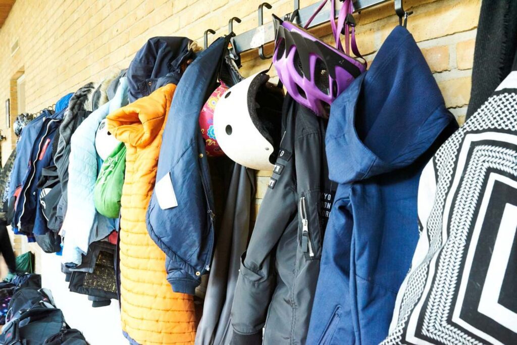 A colorful assortment of winter gear, including winter coats and helmets, is hung on a wall.