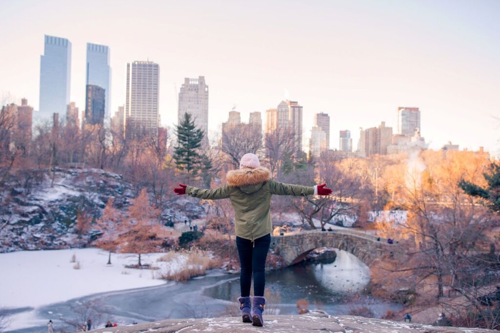 The woman enjoys the view of an ice rink and skyscrapers on a winter day in New York City.