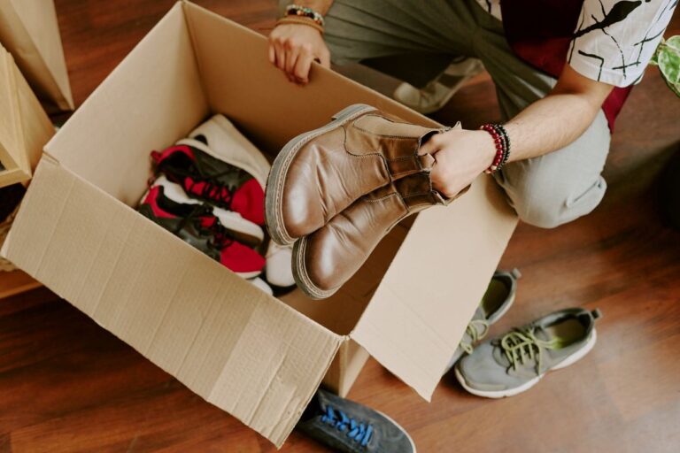 A student packing shoes and boots into a cardboard box.